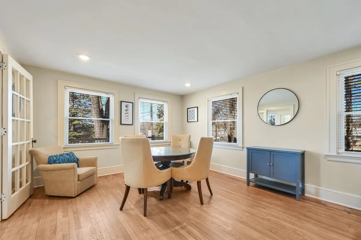 A cozy dining space with a table and chairs, mirrored wall decor, and a blue cabinet. The room is bathed in natural light, evoking a warm and inviting atmosphere for communal meals, game nights, and conversations.