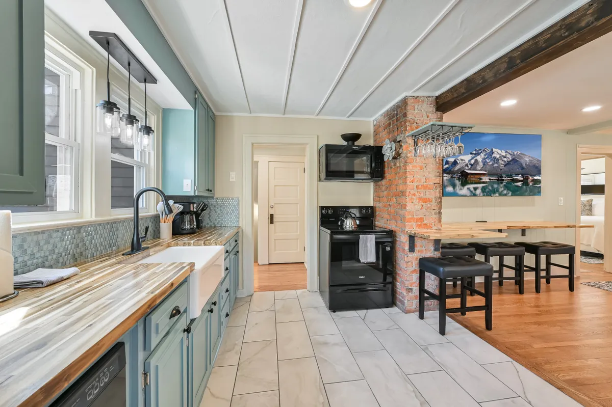 A welcoming kitchen and dining area featuring a kitchen sink with black appliances, an exposed brick wall, and an adjacent dining area. The space is open and inviting, with clear sightlines for socializing while cooking or hosting a meal.