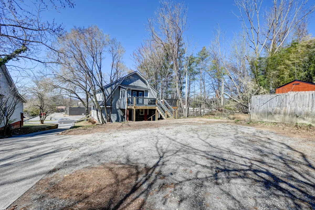 This exterior image features the Manor house surrounded by trees, with a spacious deck visible and hints of the peaceful natural setting. The deck area is inviting, suggesting a place to gather after outdoor adventures, while the greenery evokes the nearby Blue Ridge Parkway and recreational opportunities.