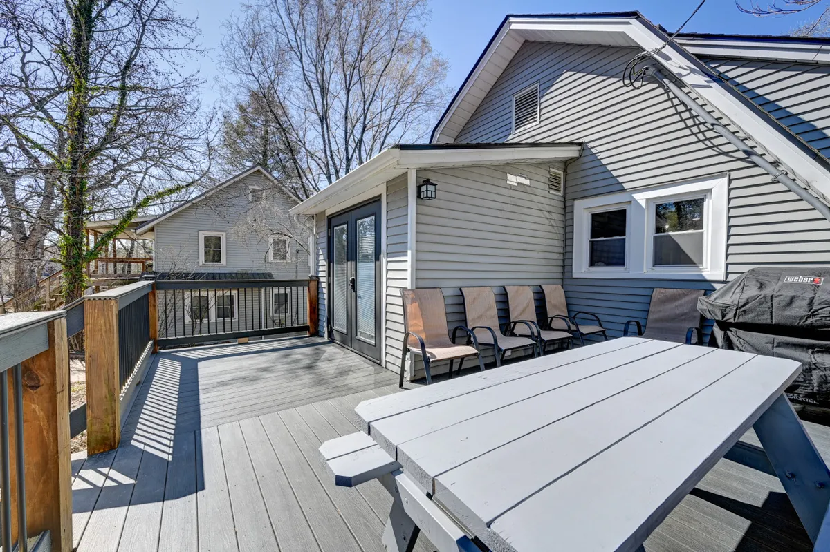 The image showcases a spacious deck with outdoor seating, an inviting table, a grill, and part of the house exterior. The vibe is casual and relaxed, ideal for al fresco dining, barbecues, and gathering with friends or family.