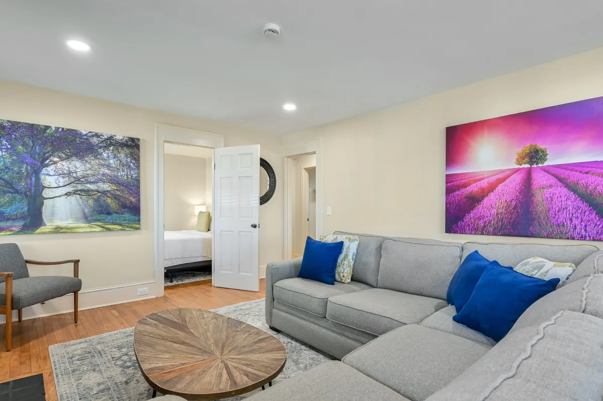 A spacious lounge area with a large sectional sofa, round wooden coffee table, and vibrant wall art. The room is designed for relaxation and socializing, providing ample space for everyone to unwind or participate in group activities.