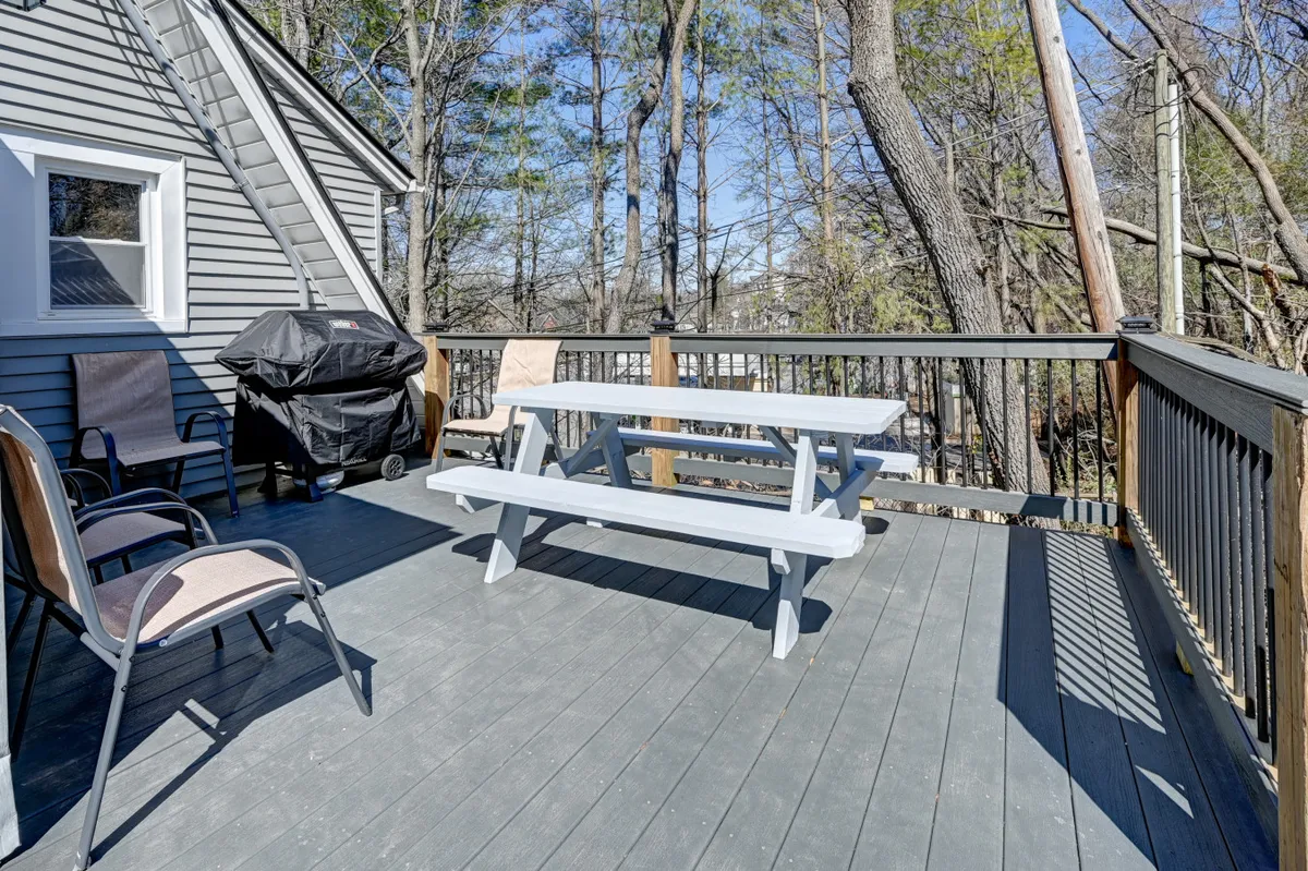 A cheerful outdoor setup featuring a picnic table, grill, and deck railing, surrounded by greenery. The scene invites outdoor dining, barbecuing, and casual gatherings with friends or family.