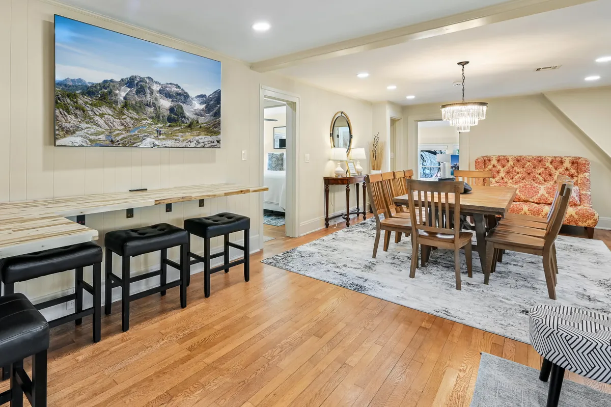 This image highlights a spacious wooden dining table surrounded by comfortable seating, with a vibrant patterned sofa and a wooden bar area with stools nearby. The overall layout invites group meals, socializing, and relaxed dining experiences.