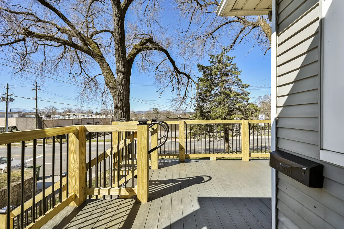 A spacious wooden deck nestled beneath a large tree, surrounded by lush greenery. The deck offers ample space for seating and gathering, with an inviting, tranquil atmosphere perfect for relaxation or socializing outdoors.